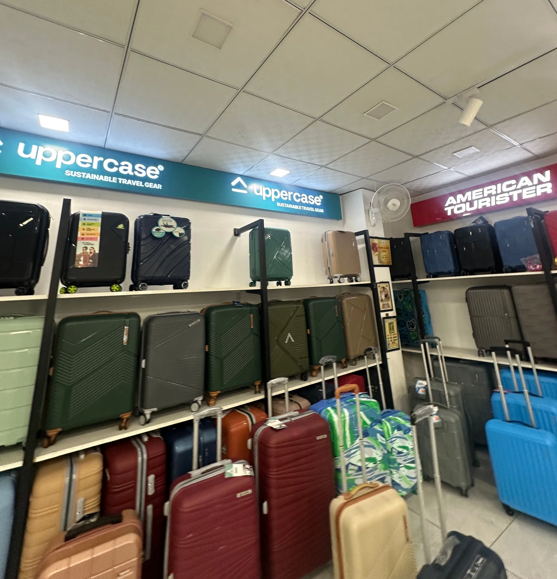 Rows of suitcases in the luggage area beneath Uppercase and American Tourister signage.